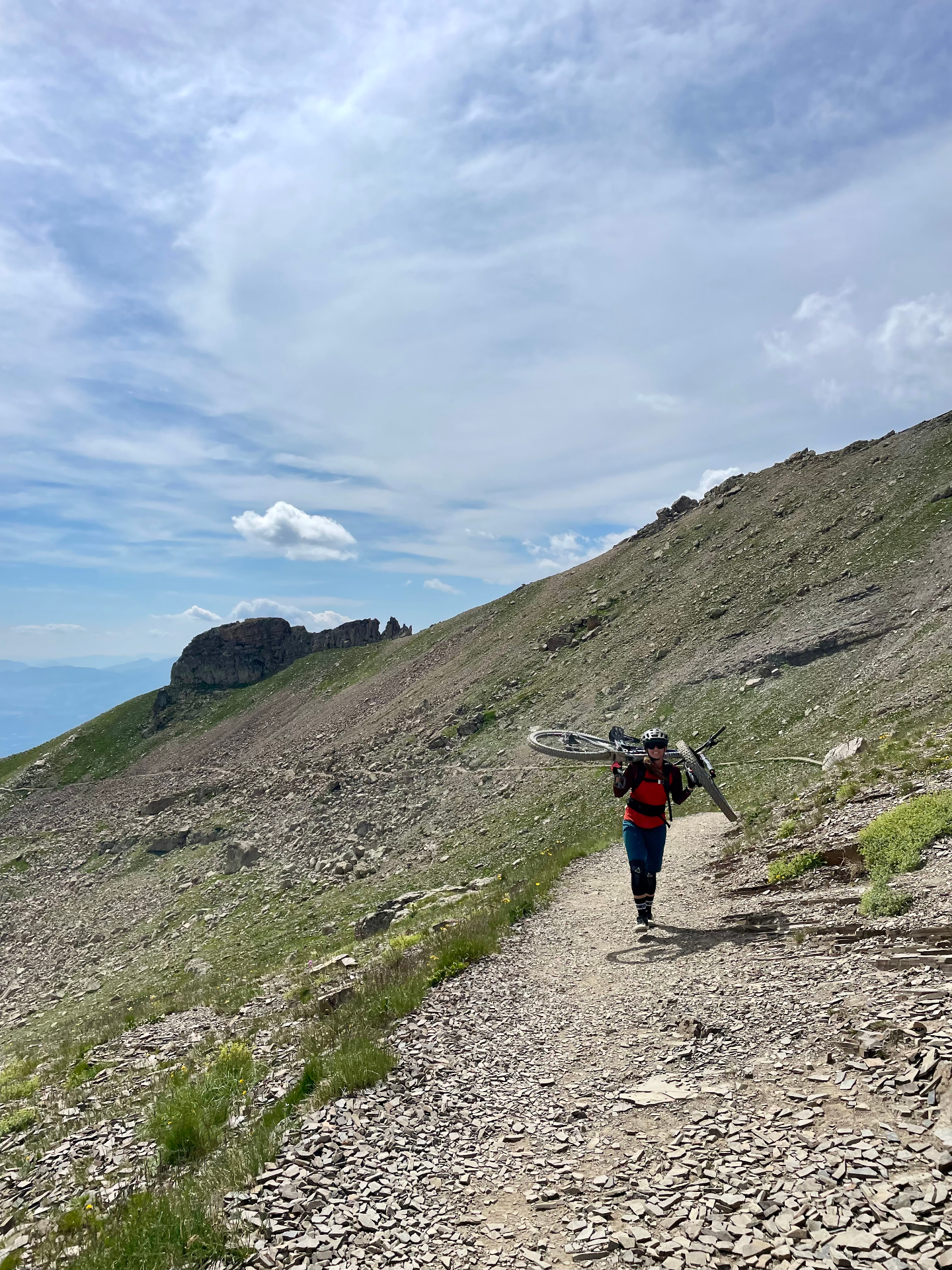 Jordan hiking up an alpine trail carrying her mountain bike